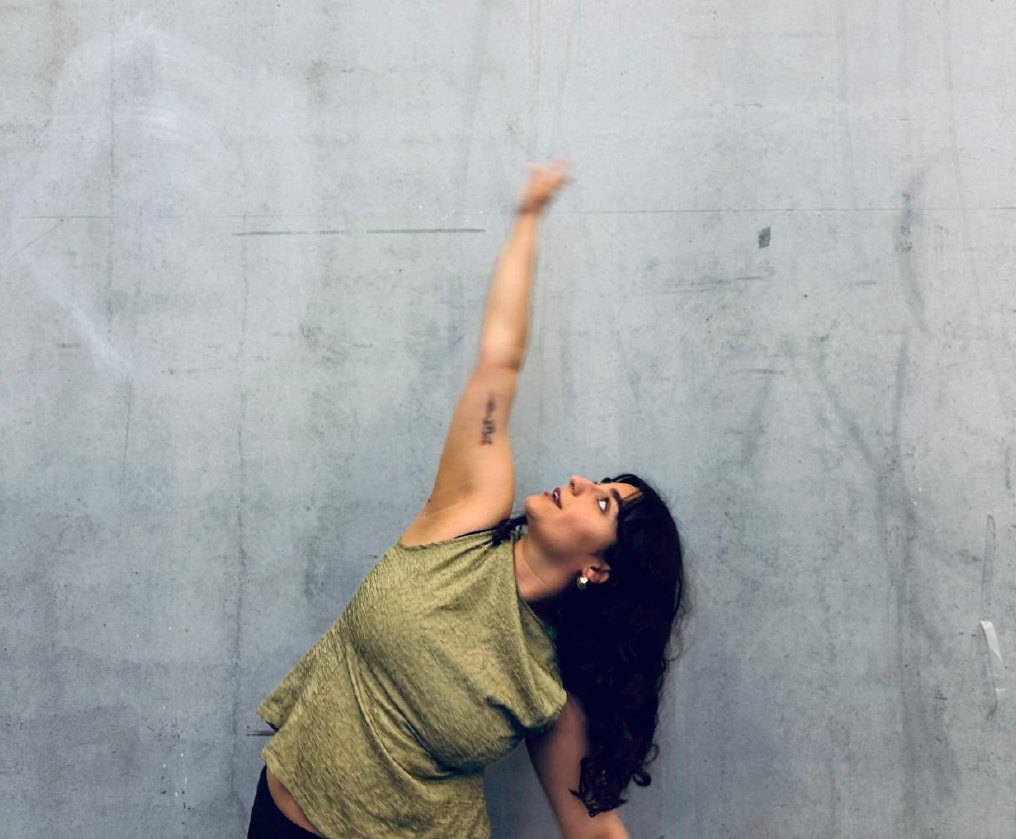 Bresa Ayub reaching upward against a concrete wall
